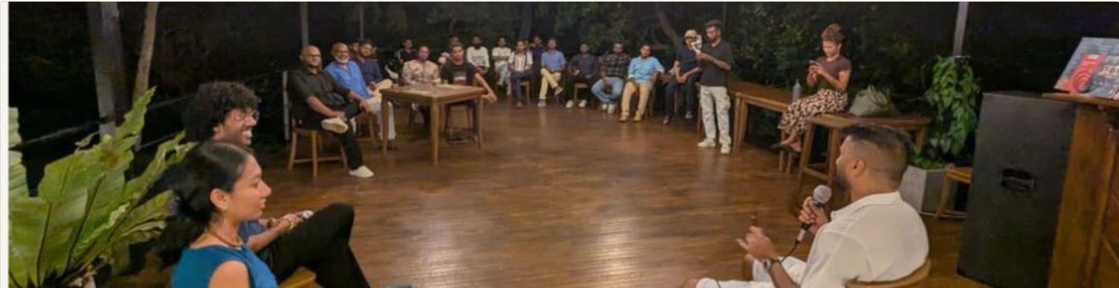A founder fireside chat on a wooden deck, speaker with microphone facing a seated circle
